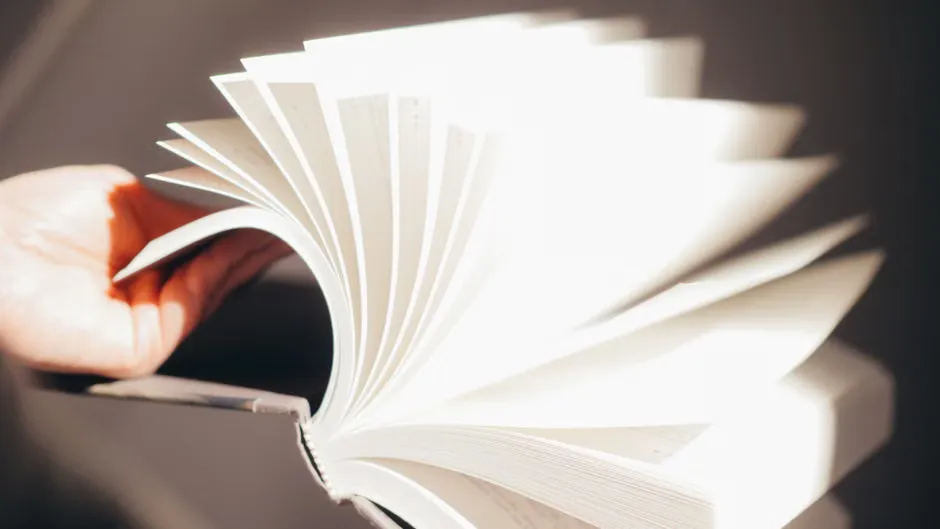 Hands turning the pages of a printed guide beside a cup of tea on soft linen, warm lamp light