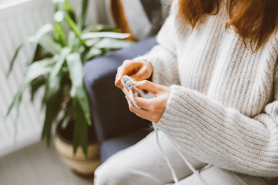 A person in a knit jumper scrolling on a phone at a kitchen table beside a cup of tea, relaxed and private